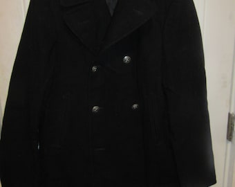 May include: A black double-breasted pea coat featuring a wide notched collar, long sleeves, and four silver-toned metallic buttons arranged in two vertical rows on the front. The coat has two vertical side pockets and a dark interior lining.