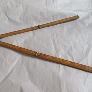 May include: A vintage wooden folding ruler, featuring brass hinges and measurement markings in inches. The ruler is a warm, light brown color and is partially open, displaying its segmented design. The ruler is approximately 36 inches long when fully extended.