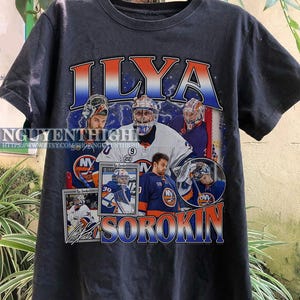 May include: Black t-shirt with a graphic print of Ilya Sorokin, a hockey player for the New York Islanders. The graphic features multiple images of Sorokin in different poses, including a close-up of his face and a full-body shot of him in his goalie gear. The graphic also includes the text "Ilya Sorokin" and "NYI".