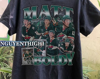 Peut inclure: T-shirt noir avec un imprimé graphique vert et blanc du joueur de hockey Matt Boldy. Le graphique comprend plusieurs images de Boldy dans différentes poses, avec le texte "Matt Boldy" imprimé en grandes lettres.