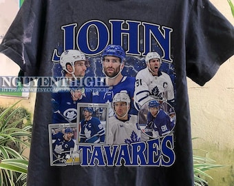 Puede incluir: Camiseta gris oscuro con un collage del jugador de hockey John Tavares en los colores azul y blanco del equipo. La camiseta incluye el nombre "JOHN TAVARES" en letras azules, con el texto de la URL de la tienda.