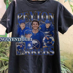 May include: Black t-shirt with a graphic of hockey player Peyton Krebs and the text "Peyton Krebs" in yellow and blue letters.