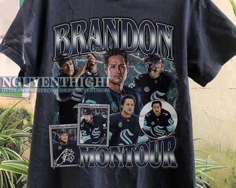 May include: Black t-shirt with a graphic of hockey player Brandon Montour. The graphic features a collage of photos of Montour in his hockey uniform, along with his name and signature.