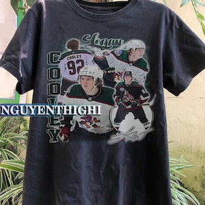 May include: Black t-shirt featuring a graphic print of hockey player Logan Cooley. The graphic includes the text "Cooley" and "Logan" and a signature.