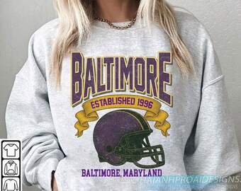 Puede incluir: Una sudadera gris jaspeado con un diseño retro. La palabra "BALTIMORE" se muestra en morado y dorado, con un casco de fútbol morado debajo. También se ve el texto "ESTABLISHED 1996" y "BALTIMORE, MARYLAND".