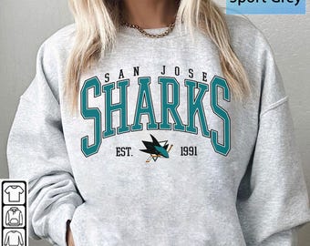 May include: Sport grey sweatshirt featuring the San Jose Sharks logo in teal and white. The logo includes the team name, a shark fin, and the establishment year, 1991. The sweatshirt is a casual, comfortable style.