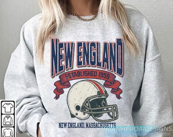 Könnte beinhalten: Hellgraues Sweatshirt mit Vintage-Grafik. Das Design zeigt die Worte "NEW ENGLAND" in Marineblau, "ESTABLISHED 1959" in Rot und einen Football-Helm. Der Text "NEW ENGLAND, MASSACHUSETTS" ist unten aufgedruckt.