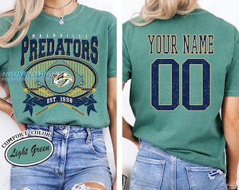 May include: Light green t-shirt featuring the Nashville Predators logo with the text "NASHVILLE PREDATORS" and "EST. 1998". The back of the shirt has the text "YOUR NAME" above the number "00". The shirt is labeled "COMFORT COLOR Light Green".