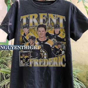May include: Black t-shirt featuring a yellow and black graphic print of hockey player Trent Frederic. The graphic includes the text "Trent Frederic" and images of hockey players wearing Boston Bruins jerseys.
