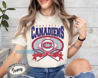 Puede incluir: Una camiseta blanca con un gráfico rojo, azul y blanco de un palo de hockey y un disco. El gráfico dice "Montreal Canadiens" y "Est. 1909".