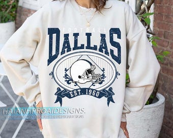Op de afbeelding: Crèmekleurige sweatshirt met een verweerde marineblauwe print. De print toont het woord "DALLAS" boven een ovaal ontwerp met een footballhelm en de tekst "EST. 1960". Een casual, sportieve stijl.