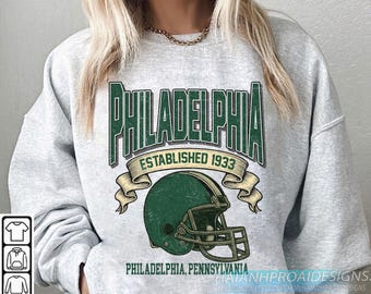 May include: A light grey sweatshirt with a green and white graphic. The graphic reads "PHILADELPHIA ESTABLISHED 1933" with a football helmet. Below the graphic is "PHILADELPHIA, PENNSYLVANIA".
