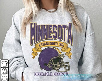 Puede incluir: Una sudadera gris con un gráfico vintage. El diseño incluye la palabra "MINNESOTA" en morado y dorado, el texto "ESTABLISHED 1961" y un casco de fútbol morado y dorado. También está presente el texto "MINNEAPOLIS, MINNESOTA".
