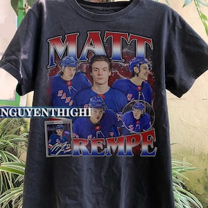 May include: Black t-shirt with a graphic print of hockey player Matt Rempe wearing a New York Rangers jersey. The graphic includes the text "MATT REMPE" and a smaller image of a hockey card with Rempe's signature.