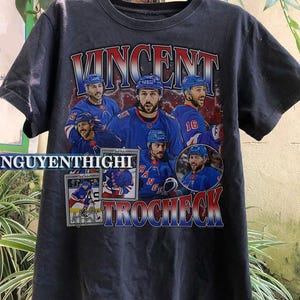 May include: Dark gray t-shirt featuring a collage of images of a hockey player in a blue uniform. The name "VINCENT TROCHECK" is printed in a distressed, vintage style across the top and bottom of the shirt.