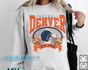 May include: Grey sweatshirt with a distressed orange and navy blue graphic that reads "FOOTBALL DENVER EST. 1969." The graphic features a football helmet and two footballs. The sweatshirt has a crew neck and long sleeves.