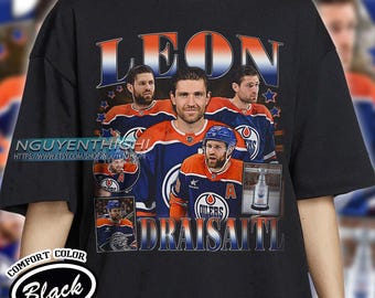 May include: Black t-shirt with a graphic of four hockey players, including Leon Draisaitl. The players are wearing their Edmonton Oilers jerseys. The text "LEON DRAISATTL" is printed in large letters across the bottom of the shirt.