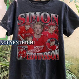 Könnte beinhalten: Schwarzes T-Shirt mit einer roten, weißen und blauen Grafik des Hockeyspielers Simon Edvinsson. Die Grafik enthält den Namen und die Nummer des Spielers sowie das Logo der Detroit Red Wings.