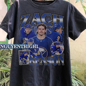 May include: Black t-shirt with a graphic of hockey player Zach Benson wearing a blue and gold jersey with the number 9. The text "Zach Benson" is printed in yellow and blue on the shirt.
