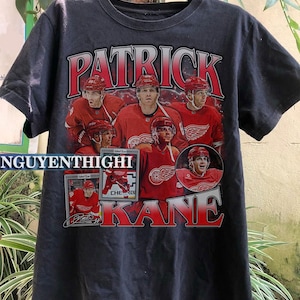 May include: Black t-shirt with a red, white, and blue graphic of hockey player Patrick Kane. The graphic includes the text "Patrick Kane" and a collage of hockey cards.