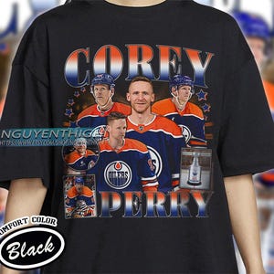 May include: Black t-shirt with a retro design featuring hockey player Corey Perry. The graphic includes the player's name, team logo, and action shots. The shirt also has the text "COMFORT COLOR" and "Black".