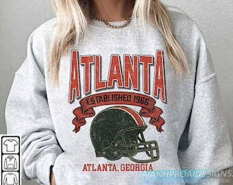 Puede incluir: Sudadera gris claro con un diseño desgastado. Presenta la palabra "ATLANTA" en rojo, un casco de fútbol americano y el texto "ESTABLISHED 1966". Debajo, "ATLANTA, GEORGIA".