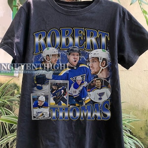 May include: Black t-shirt featuring a graphic print of hockey player Robert Thomas. The graphic includes multiple images of Thomas in his St. Louis Blues uniform, including a hockey card.