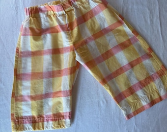 May include: A pair of pants featuring a plaid pattern in shades of yellow, orange, and white. The pants have an elasticized waistband and a straight-leg cut, constructed from a lightweight fabric with visible stitching along the hemline.