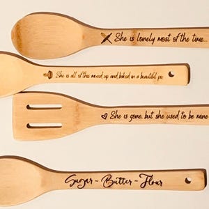 May include: Set of four wooden spoons with engraved sayings. The spoons are made of natural bamboo and have a light brown color. The sayings on the spoons are: "She is lonely most of the time...", "She is all of this mixed up and baked on a beautiful pie", "She is gone, but she used to be mine", and "Sugar - Butter - Flour".