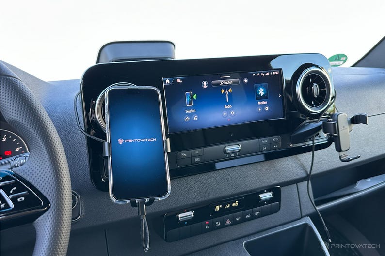 K&ouml;nnte beinhalten: Ein Smartphone, das in einem Auto montiert ist und das Logo "PRINTIVATECH" anzeigt. Das Telefon ist mit einem Ladekabel verbunden. Das Armaturenbrett des Autos verf&uuml;gt &uuml;ber ein digitales Display mit Radio- und Bluetooth-Optionen.