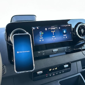 K&ouml;nnte beinhalten: Ein Armaturenbrett im Auto mit einem Smartphone in einer transparenten H&uuml;lle, das am Armaturenbrett befestigt ist. Das Telefon zeigt das Printovatech-Logo an. Das Armaturenbrett hat ein digitales Display mit Radio- und Telefonoptionen.