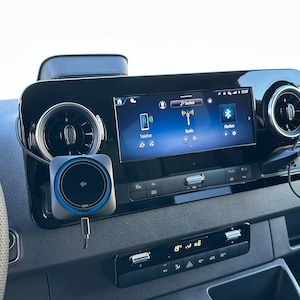 K&ouml;nnte beinhalten: Fahrzeug-Armaturenbrett mit zentralem Infotainment-Bildschirm, der Telefon-, Radio- und Bluetooth-Symbole anzeigt. Ein kabelloses Ladepad und eine Telefonhalterung sind am Armaturenbrett montiert. Das Armaturenbrett ist schwarz mit silbernen Akzenten.