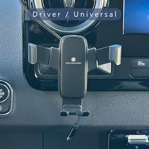 K&ouml;nnte beinhalten: Ein schwarzer Printovatech-Telefonhalter, der in einem Auto montiert ist. Der Halter ist am Armaturenbrett befestigt und verf&uuml;gt &uuml;ber verstellbare Arme zur Sicherung eines Telefons. Das Armaturenbrett des Autos umfasst eine Start/Stopp-Taste und einen Bildschirm.