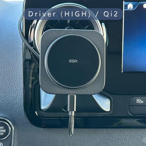 K&ouml;nnte beinhalten: Ein schwarzes ESR kabelloses Telefonladeger&auml;t, das im Armaturenbrett eines Autos montiert ist. Das Ladeger&auml;t ist quadratisch mit einem kreisf&ouml;rmigen Ladebereich. Der Infotainment-Bildschirm des Autos zeigt ein Telefonsymbol und das Wort "Telefon". Der Text "Driver (HIGH) / Qi2" ist sichtbar.