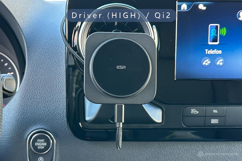 K&ouml;nnte beinhalten: Ein schwarzes ESR kabelloses Telefonladeger&auml;t, das im Armaturenbrett eines Autos montiert ist. Das Ladeger&auml;t ist quadratisch mit einem kreisf&ouml;rmigen Ladebereich. Der Infotainment-Bildschirm des Autos zeigt ein Telefonsymbol und das Wort "Telefon". Der Text "Driver (HIGH) / Qi2" ist sichtbar.