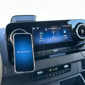 K&ouml;nnte beinhalten: Ein Armaturenbrett im Auto mit einem Smartphone in einer transparenten H&uuml;lle, montiert neben einem digitalen Display. Das Telefon zeigt das Printovatech-Logo auf blauem Farbverlauf. Das Armaturenbrett hat auch L&uuml;ftungsd&uuml;sen und Klimaanlagen.