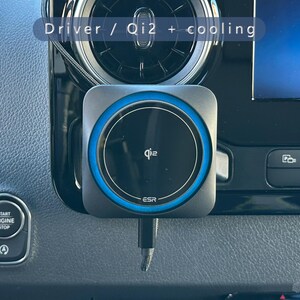 K&ouml;nnte beinhalten: Ein schwarzes und graues Qi2-Wireless-Ladeger&auml;t mit blauem Akzentring ist im Armaturenbrett eines Autos montiert. Das Ladeger&auml;t hat das ESR-Logo und den Text "Driver / Qi2 + cooling". Das Armaturenbrett des Autos verf&uuml;gt au&szlig;erdem &uuml;ber eine Start/Stopp-Taste und einen Bildschirm mit der Aufschrift "Telefon".