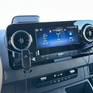 Könnte beinhalten: Armaturenbrett eines Fahrzeugs mit zentralem Bildschirm, der eine Benutzeroberfläche mit Symbolen für Telefon, Radio und Bluetooth anzeigt. Das schwarze Armaturenbrett umfasst Lüftungsschlitze und eine digitale Temperaturanzeige. Eine Telefonhalterung ist angebracht.
