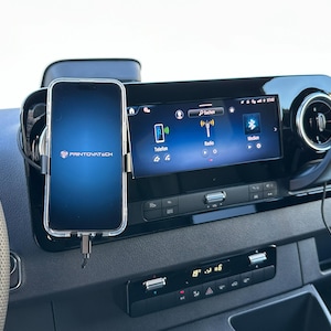 K&ouml;nnte beinhalten: Ein Armaturenbrett im Auto mit einem Smartphone in einer transparenten H&uuml;lle, das &uuml;ber ein Ladekabel angeschlossen ist. Das Telefon zeigt einen blauen Bildschirm mit dem Printovatech-Logo. Ein digitales Display zeigt Radio- und Bluetooth-Optionen. Das Armaturenbrett ist schwarz.