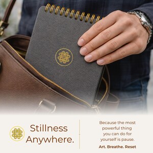 Puede incluir: Un cuaderno de espiral gris oscuro con un emblema de nudo circular dorado en la portada. El texto en la imagen dice: Stillness Anywhere. Because the most powerful thing you can do for yourself is pause. Art. Breathe. Reset.