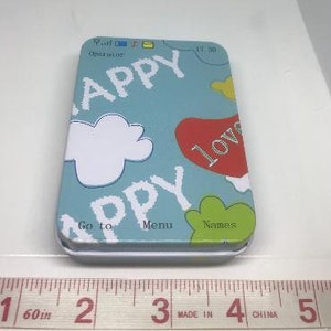 Puede incluir: Una lata azul con una nube blanca, las palabras "Happy", "Go to", "Menu" y "Names", y un coraz&oacute;n rojo con la palabra "Love" en ella.