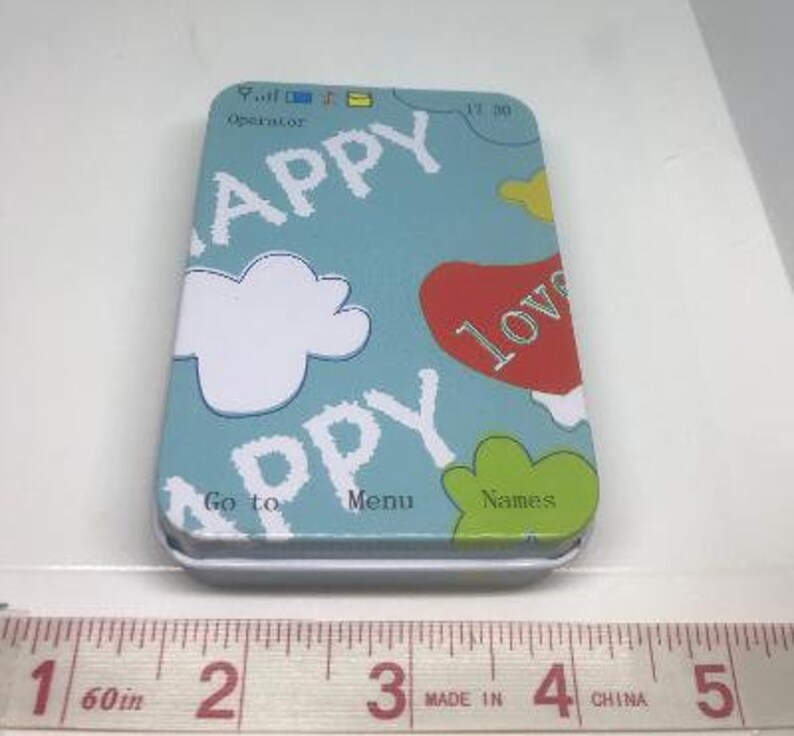 Puede incluir: Una lata azul con una nube blanca, las palabras "Happy", "Go to", "Menu" y "Names", y un coraz&oacute;n rojo con la palabra "Love" en ella.