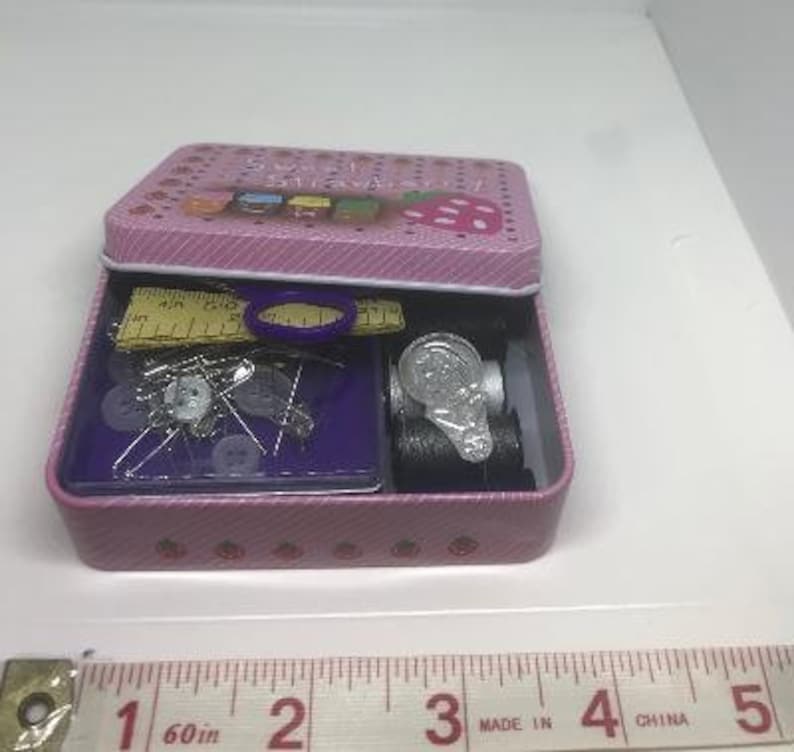 Puede incluir: Un kit de costura rosa con un dise&ntilde;o de fresa. El kit incluye agujas, hilo, botones y una regla. El kit est&aacute; etiquetado como "Sweet Sews".