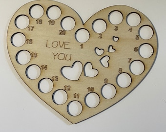 May include: Wooden heart-shaped yarn holder with 20 numbered holes and the words "LOVE YOU" inscribed on the surface.