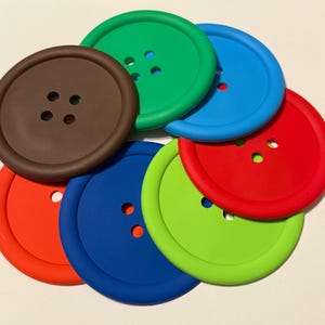 Puede incluir: Conjunto de seis posavasos de silicona con forma de botón. Los posavasos son de color marrón, verde, azul, rojo y naranja.