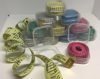 May include: A collection of small, clear plastic cases containing colorful measuring tapes. The tapes are wound up inside the cases and are ready to be used for measuring fabric, crafts, or other projects.
