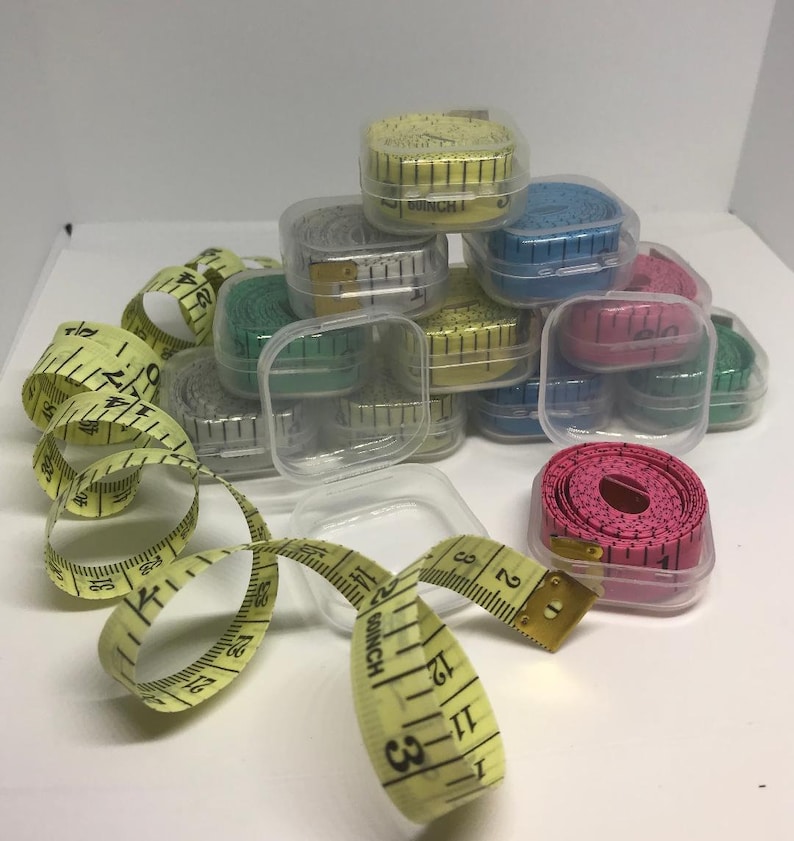 May include: A collection of small, clear plastic cases containing colourful measuring tapes. The tapes are wound up inside the cases and are ready to be used for measuring fabric, crafts, or other projects.