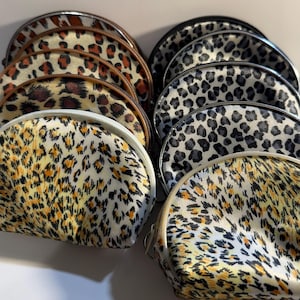 May include: A collection of small, semi-circular cosmetic bags with a leopard print design. The bags feature a variety of colors, including black, white, brown, and yellow. Each bag has a zipper closure and a contrasting trim.