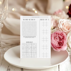May include: A white rectangular game card featuring a word search puzzle, a Sudoku grid, and a Best of 5 tic-tac-toe section. The top text reads Saturday March 21, 2025. The word search includes terms like Love, Marriage, Honeymoon, and Dancing.