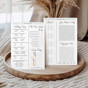 Pode incluir: Dois cart&otilde;es de atividades de casamento brancos com texto e gr&aacute;ficos pretos. O cart&atilde;o esquerdo inclui um quiz de casamento, o jogo dos sapatos e m&uacute;sicas com emojis. O cart&atilde;o direito apresenta grelhas de jogo do galo, um labirinto e um ca&ccedil;a-palavras.